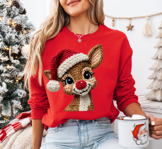Woman wearing a red sweatshirt with a reindeer design, holding a mug in a festive setting.